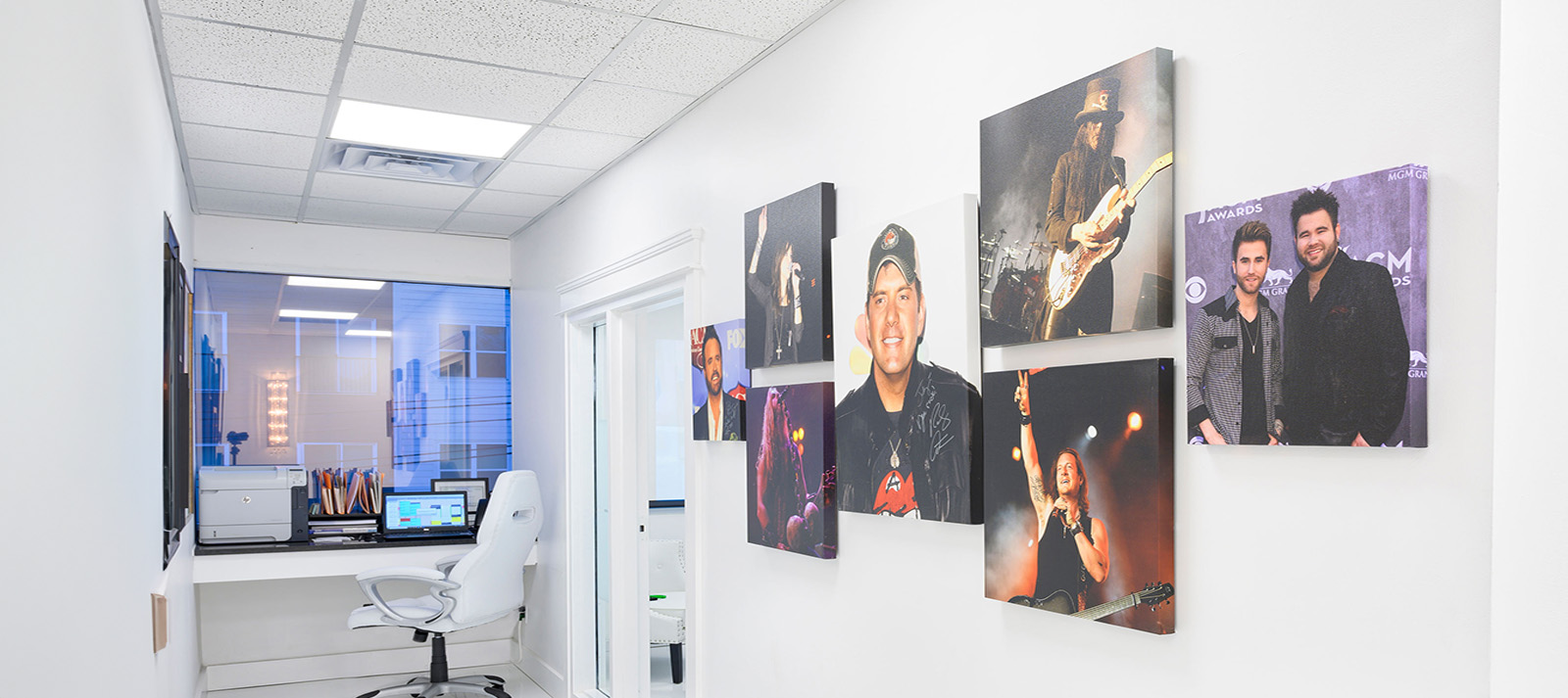 The image shows an interior office space with a large wall displaying framed photographs of individuals, some of whom are musicians, and a modern desk area visible at the forefront.