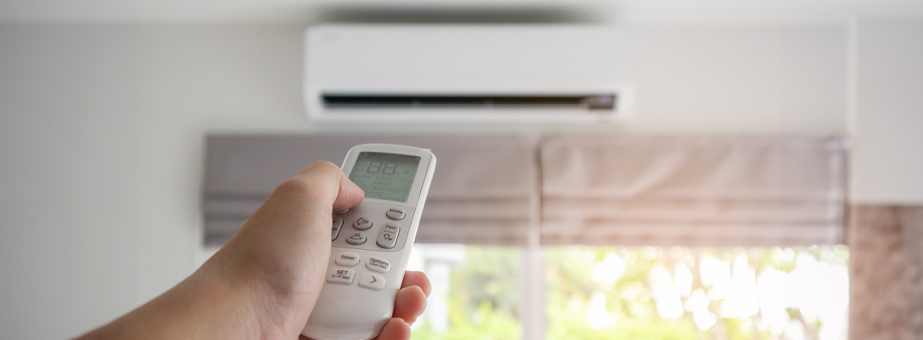 An individual s hand holding a remote control pointed at an air conditioning unit set into a window.