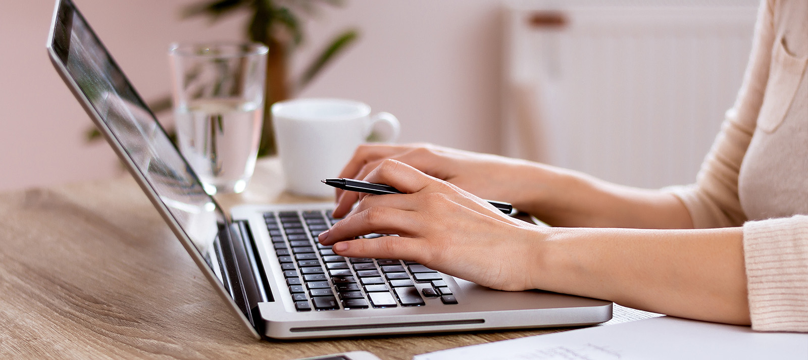 Woman typing on laptop at desk with coffee cup.
