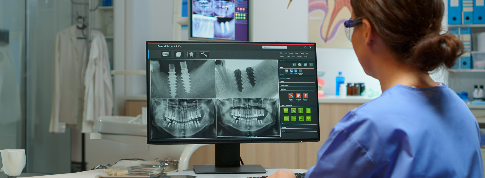 A medical professional is seated at a workstation with a large monitor displaying an X-ray image, while another smaller monitor shows a patient s face with vital signs information.