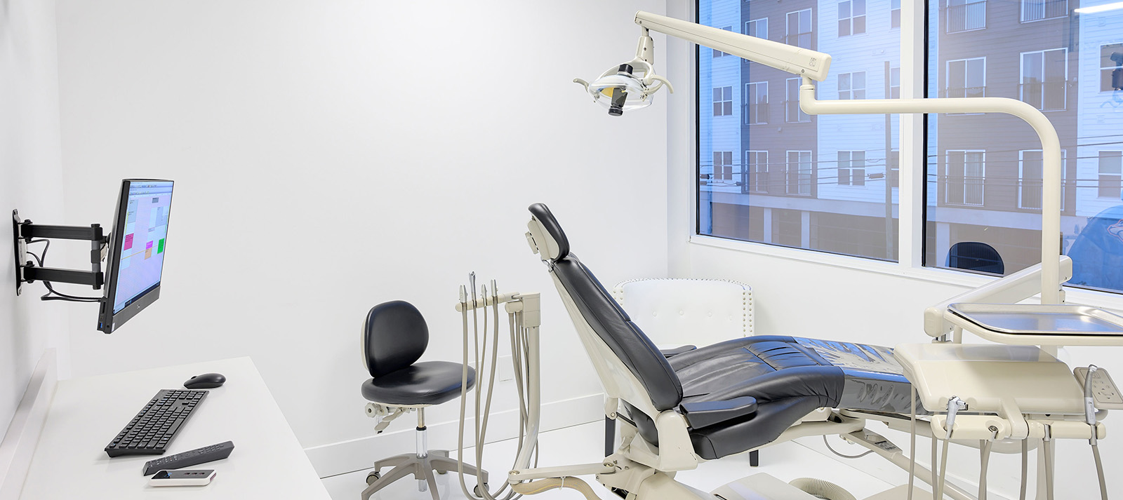 The image shows a dental office interior with various equipment including chairs, monitors, and a desk, all set up for patient care and treatment.