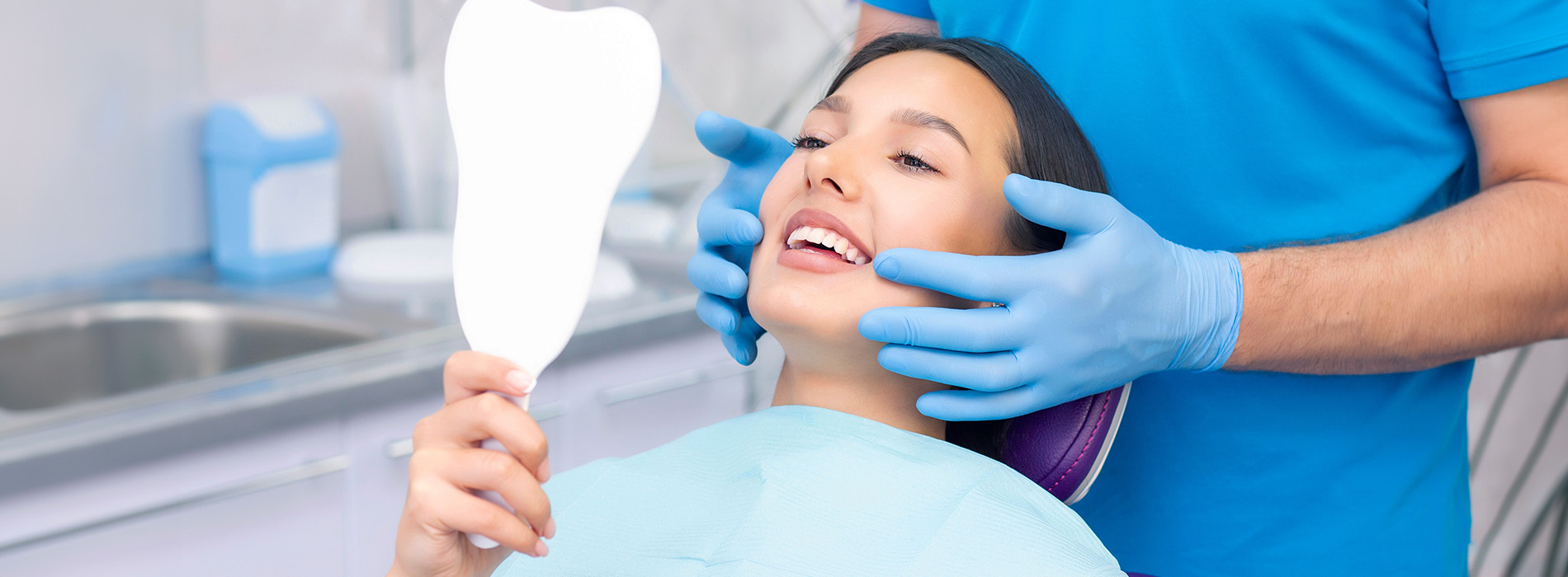 A dental hygienist holding a mirror while examining a patient s teeth.
