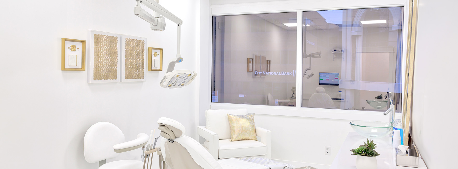 The image shows a modern interior space with a clean, minimalistic design featuring a white color scheme, a large window with a view of the outdoors, and a well-appointed room that includes a seating area with a chair and a table, as well as a sleek wall-mounted mirror.
