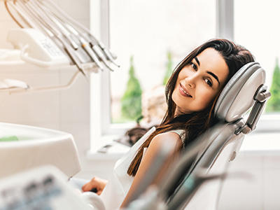 A woman sitting in a dental chair with a smile, looking towards the camera, in a dental office setting.