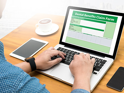 A person using a laptop with a document titled  Dental Benefits Claim Form  displayed on the screen.