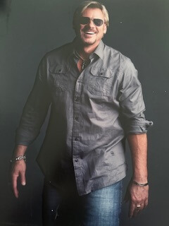 The image shows a man with sunglasses standing against a gray background.