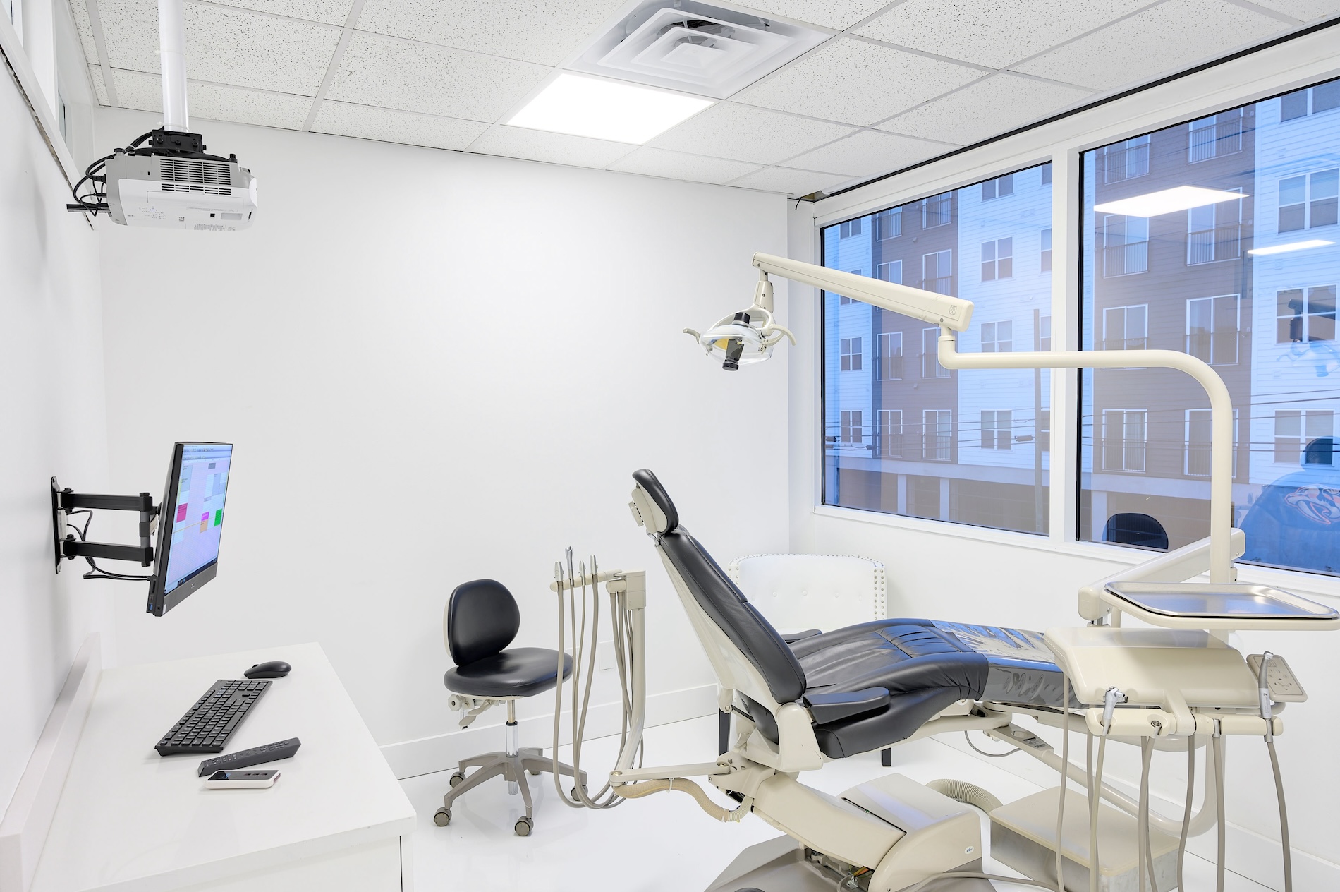 The image shows a modern dental office interior with a clean and well-organized appearance, featuring dental chairs, equipment, and a desk with a computer monitor, keyboard, and mouse.