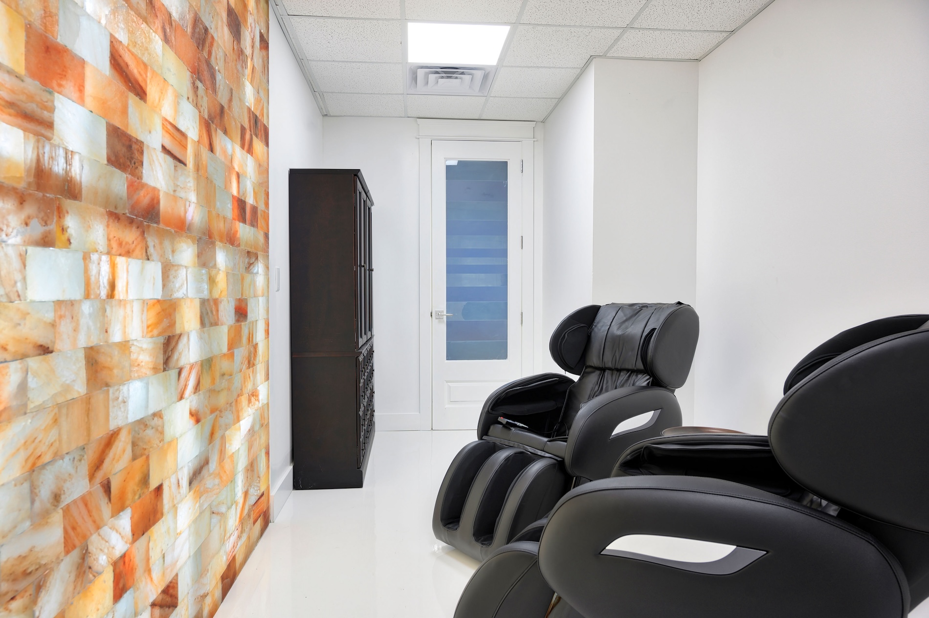 The image shows an interior space featuring a modern chair with a backrest, a large, colorful wall decoration resembling a rock formation, and a section of a waiting area with a single chair visible.