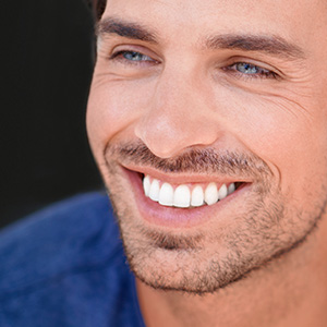 A smiling man with short hair and a beard, wearing a blue shirt, against a dark background.