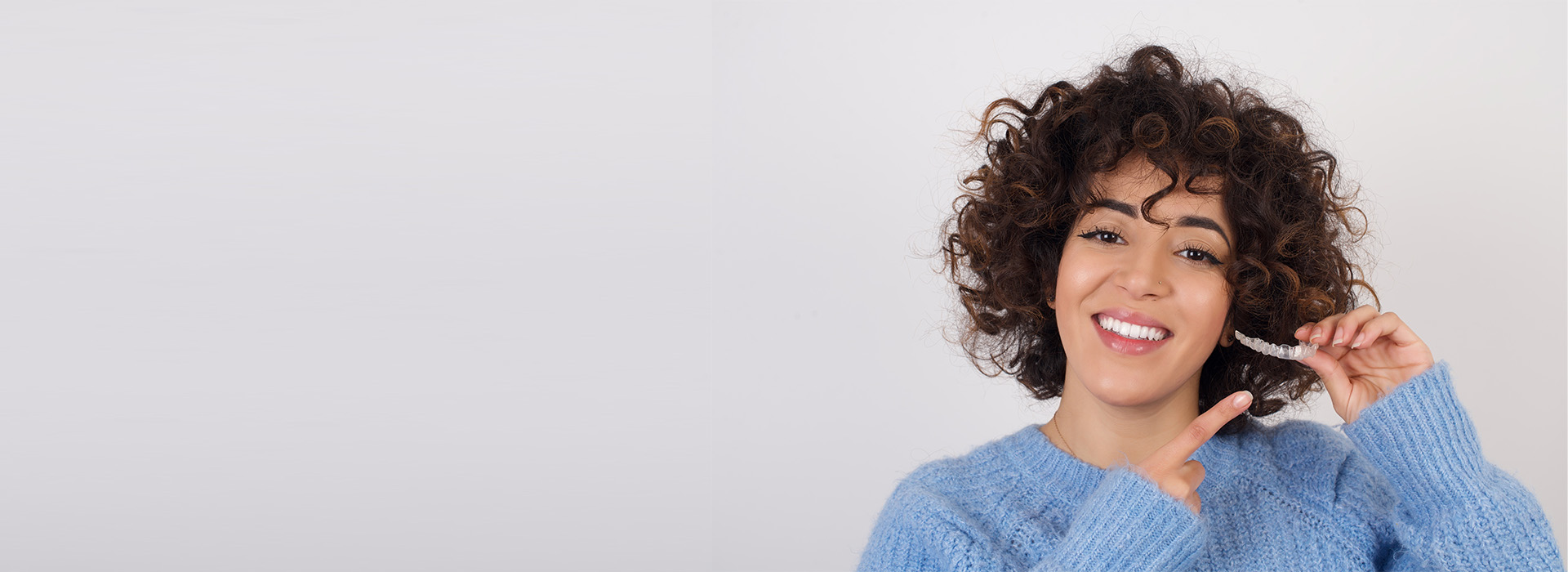 A woman with short curly hair smiling at the camera against a plain background.