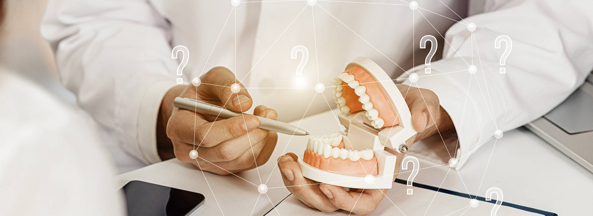 The image shows a person holding a model of a human mouth with teeth, using a tablet computer to view detailed information about dental implants.