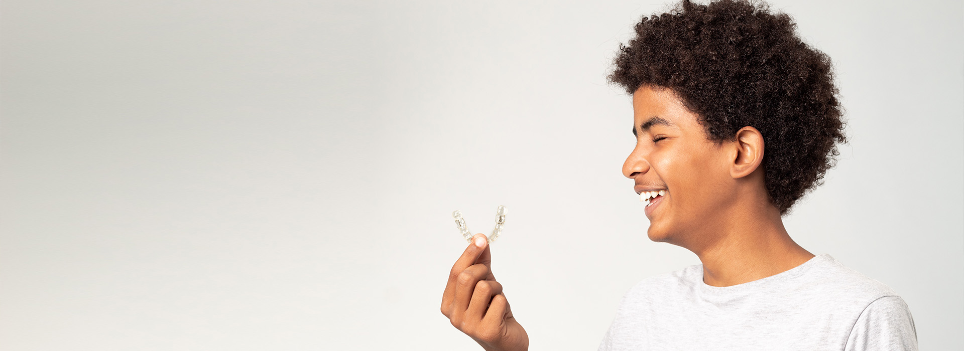 The image shows a person holding a small bird with both hands, smiling at the camera while standing against a plain background.