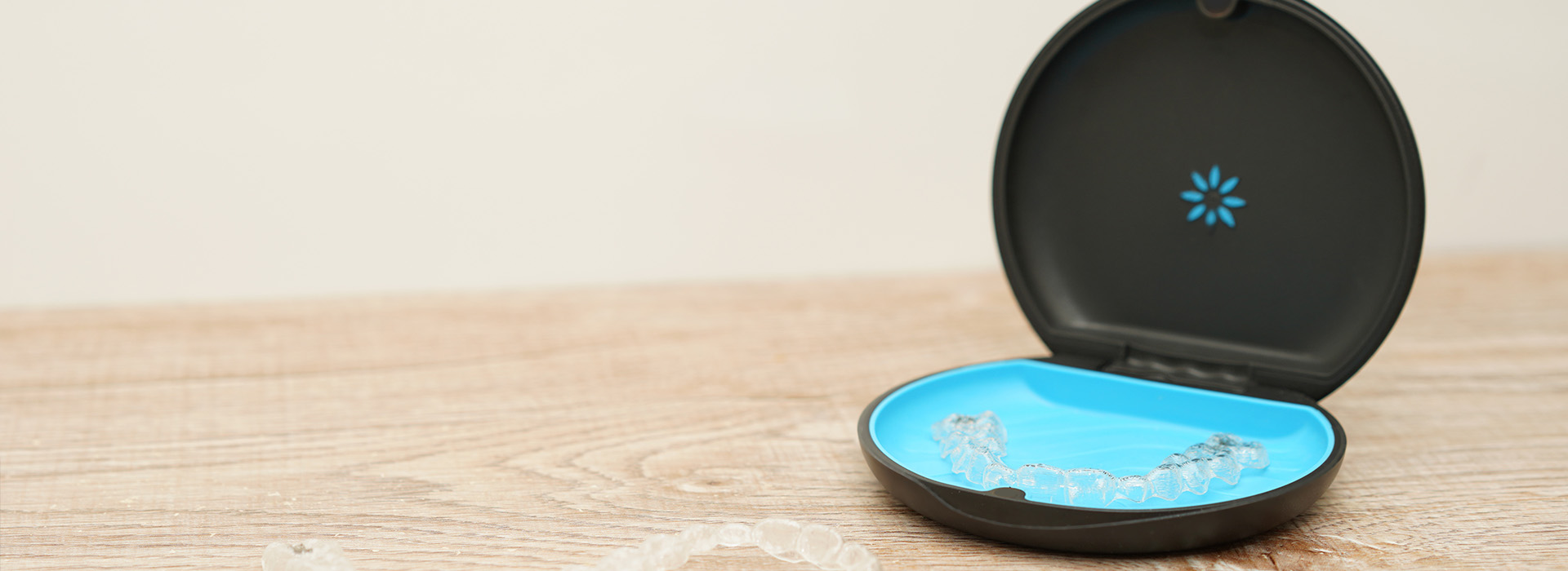 The image shows a small, round, blue object with a white logo on its side placed on a wooden surface, next to a black smart home device.
