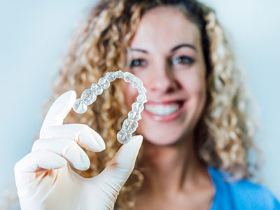 A woman holding up a clear plastic dental retainer with a smile.