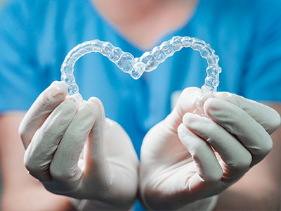 A person wearing gloves holds up a transparent heart-shaped object with clear braces inside, symbolizing dental health.