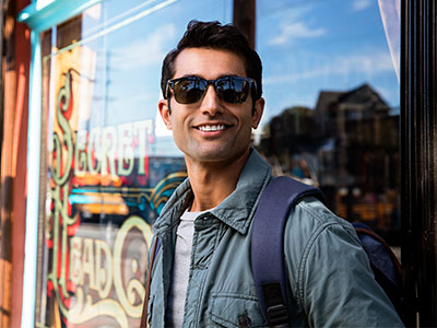 A man wearing sunglasses and a backpack stands in front of a store window with a sign that reads  Sin City .
