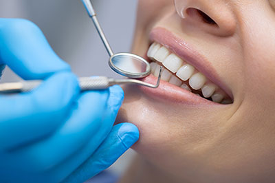 The image shows a person receiving dental care, with a dental professional using tools on their teeth while wearing protective gloves and a face mask.