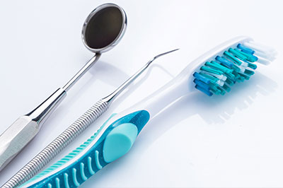 An image featuring dental instruments such as scissors and a toothbrush on a white background with a blue toothpaste tube nearby.