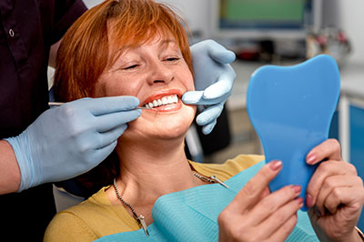 A woman in a dental chair receiving teeth cleaning service from a dental hygienist, with a smile on her face.