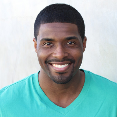 An elderly couple with white hair, smiling at each other, posing for a photo outdoors during daylight.