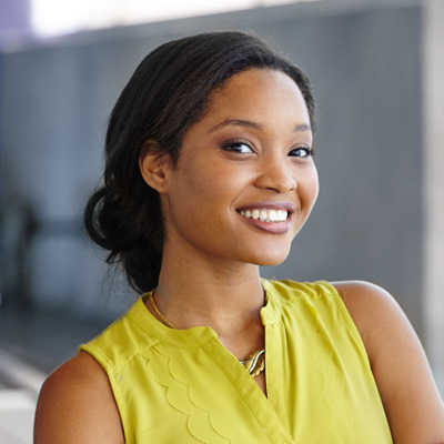 A smiling woman with dark hair wearing a yellow top stands against a backdrop.