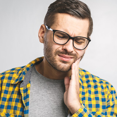 A man wearing glasses and a plaid shirt, with his hand on his chin, appears to be in pain or discomfort, possibly due to toothache.