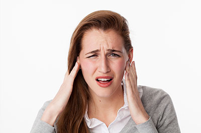 A woman with her hand on her head, possibly in pain or discomfort, against a white background.