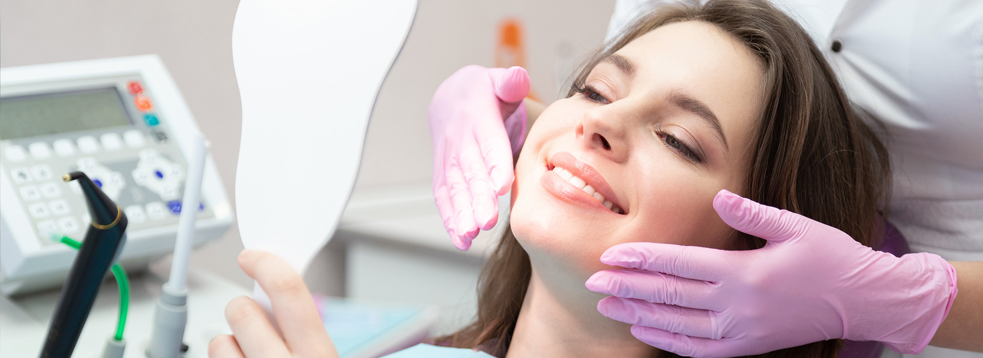 A woman receiving dental treatment with a dentist using a handheld device on her mouth.