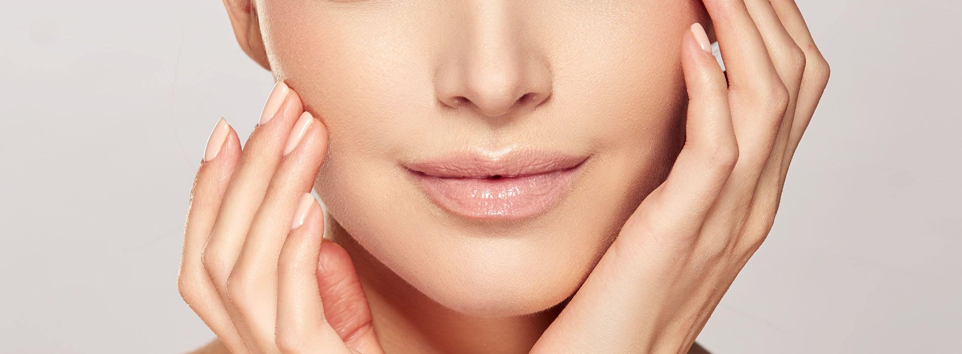 A woman s face with a focus on her eyes, nose, and hands gently placed on her cheeks, set against a white background.