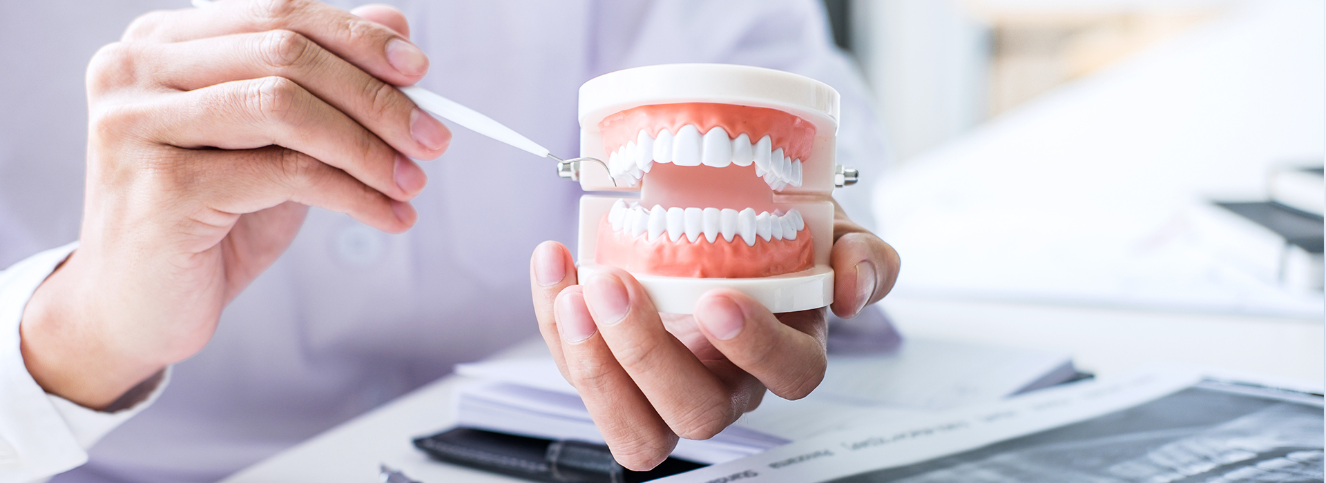 A person s hand holding a toothbrush over a cup of water with a red gum line on it, set against a blurred office background.