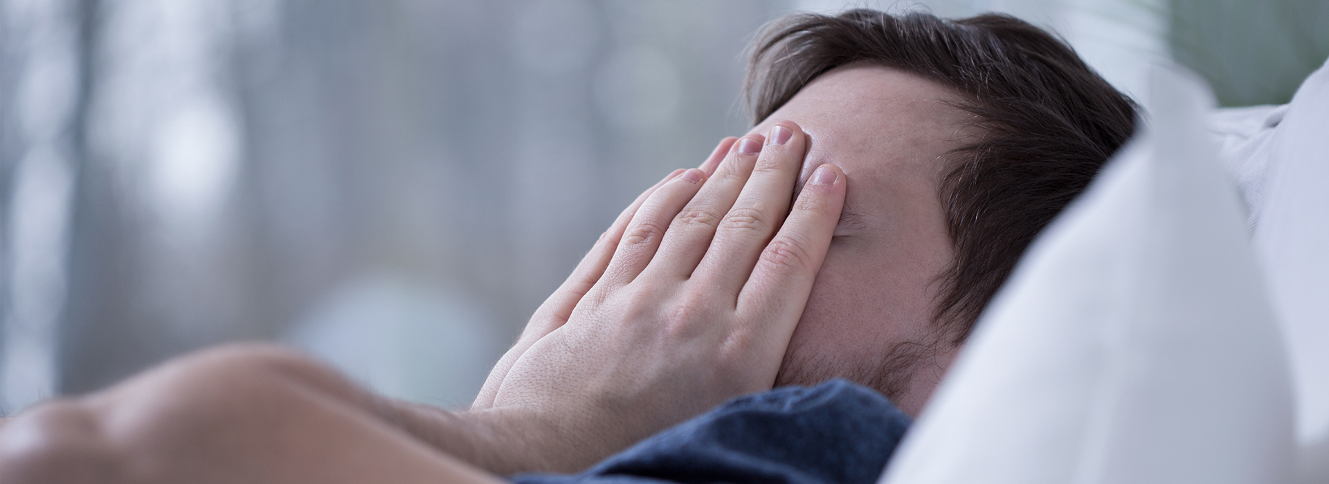 Man lying on bed with hand covering face, appearing to be asleep or resting.