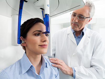 The image shows a person sitting in front of a 3D scanner with a medical professional standing beside them, observing the scan on a screen.
