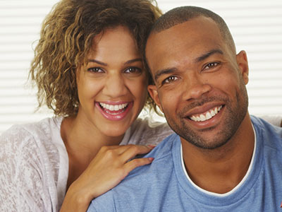 A smiling couple posing together with one arm around the other s shoulder.