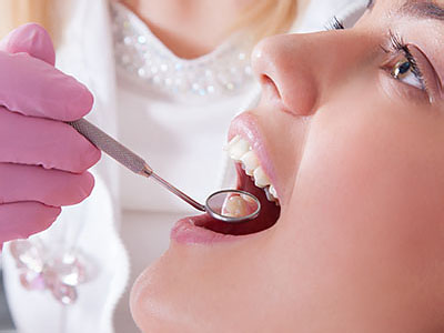 A dental hygienist is cleaning a woman s teeth using a dental pick.