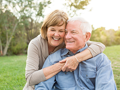 An older man and woman embrace each other outdoors during daylight.