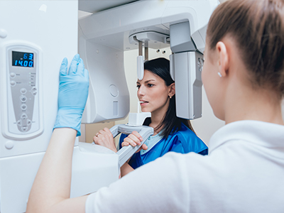 The image shows two individuals, likely healthcare professionals, working with medical imaging equipment, with one person standing beside a large digital display and another interacting with the equipment.