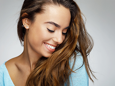 The image features a smiling woman with long brown hair, wearing a light blue top, looking slightly away from the camera with her head turned over her shoulder.