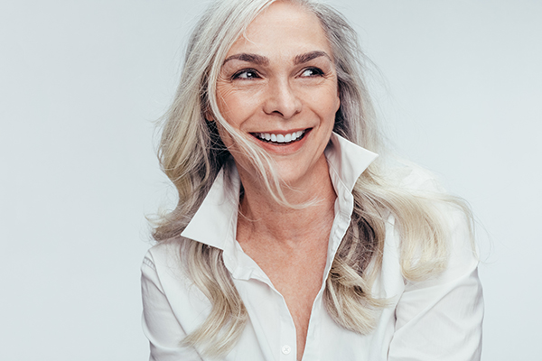 A woman with short blonde hair is smiling at the camera, wearing a white shirt.