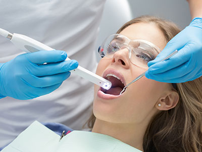 A dental professional using a digital device to inspect a woman s teeth during a dental appointment.