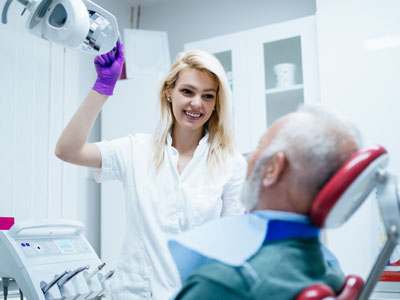 A female dental hygienist assisting an elderly patient with a tooth cleaning procedure.