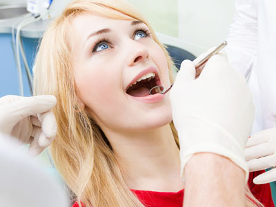 A woman receiving dental care with her mouth open, surrounded by medical professionals wearing white gloves and coats.