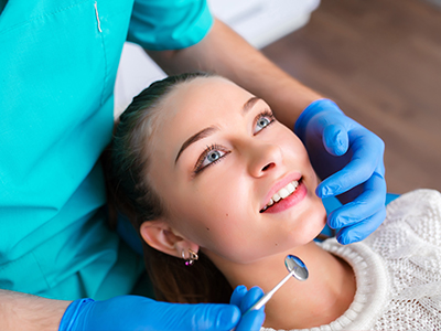 An image depicts a dental hygienist performing a teeth cleaning procedure on a patient s mouth, with the patient sitting comfortably in a dental chair and wearing protective eyewear.