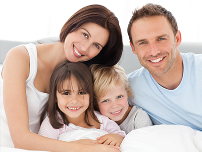 The image shows a family of four with two adults and two children posing together on a bed.