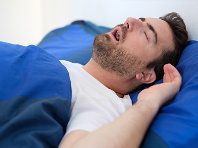 The image shows a man lying in bed with his eyes closed, appearing to be asleep.